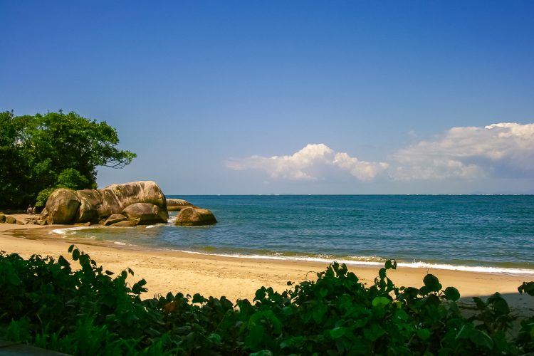 uma praia arenosa com um afloramento rochoso na água