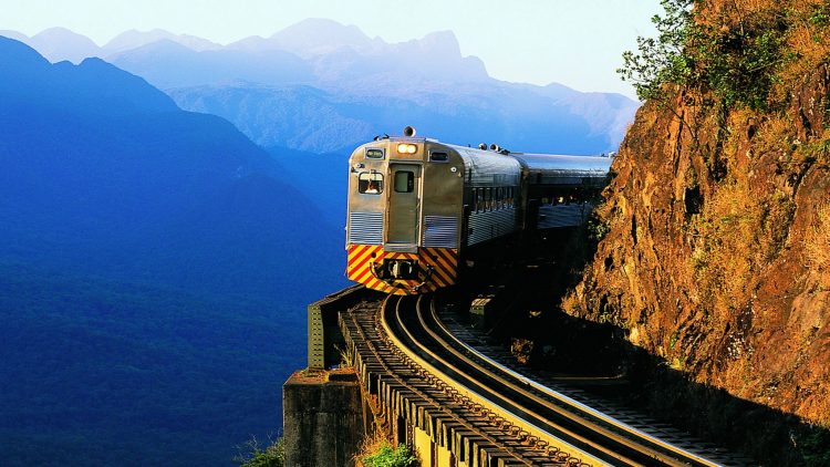 um trem prateado viajando pelos trilhos próximo a uma montanha