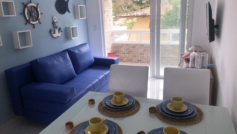 Sala com sofá cama, tv, mesa para refeições e varanda externa